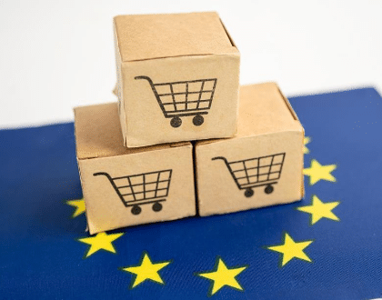 3 petits cartons ornés d'un logo de caddie sont posés en forme de pyramide sur le drapeau européen, pour illustrer le nouveau règlement européen sur les emballages.