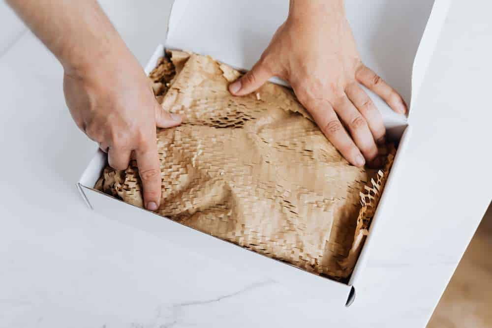 Deux mains ajustant un papier de protection dans un carton d'emballage.