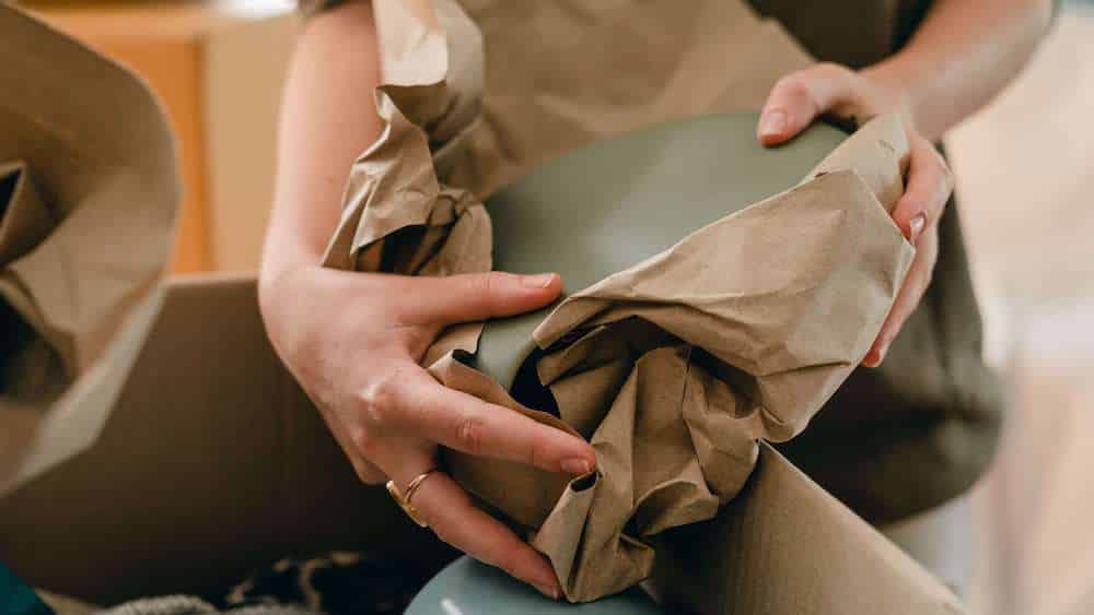Mains tenant une assiette partiellement emballée dans une papier de protection, au-dessus d'un carton.